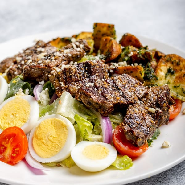 A vibrant Eden Table steak salad with hard-boiled eggs, tomatoes, red onions, and roasted potatoes.