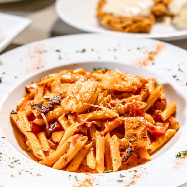 Close-up of penne pasta with shrimp, chicken, and tomato sauce, garnished with cheese and herbs.