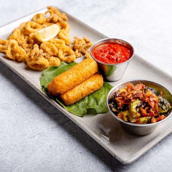 A platter of fried calamari, mozzarella sticks, roasted brussels sprouts with bacon, and marinara sauce.