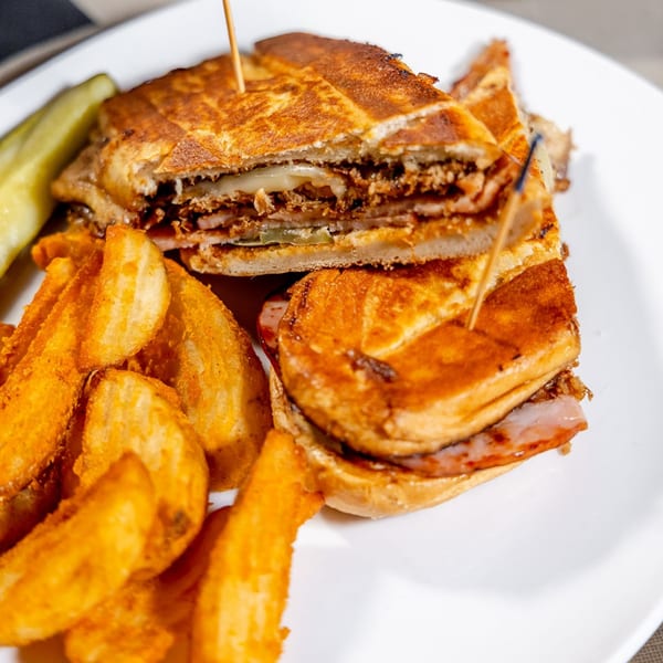 Cuban sandwich with melted cheese, pulled pork, ham, and pickles, served with seasoned potato wedges.