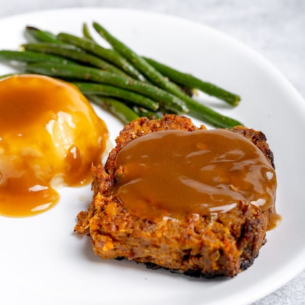 Meatloaf with gravy, mashed potatoes, and green beans on a white plate.